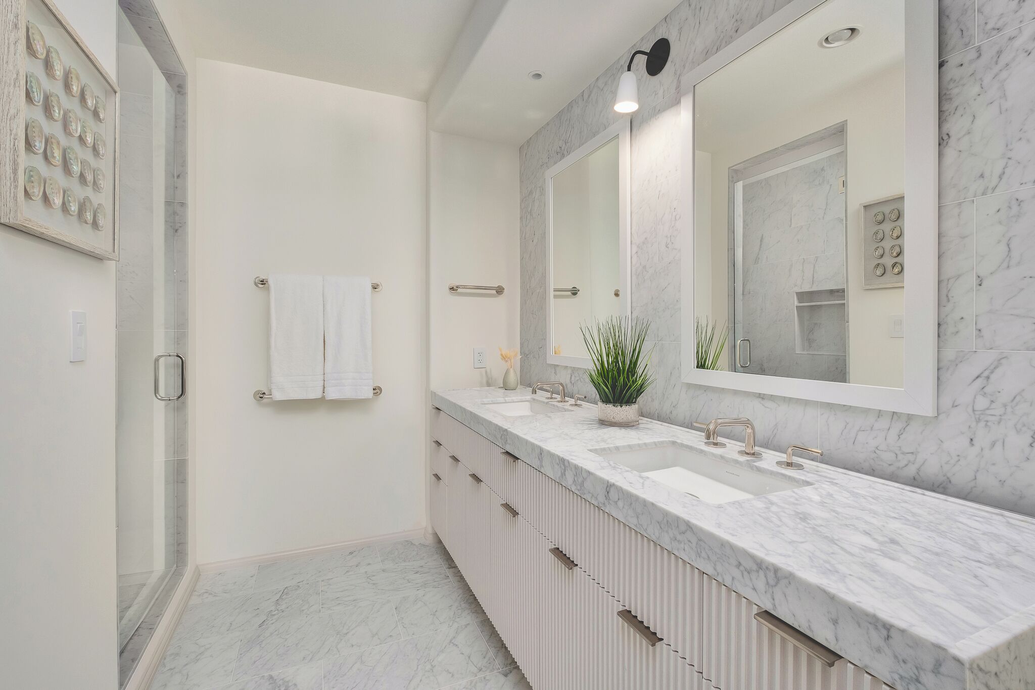 Un baño moderno con un amplio mostrador de mármol, un espejo grande y una cabina de ducha de vidrio.