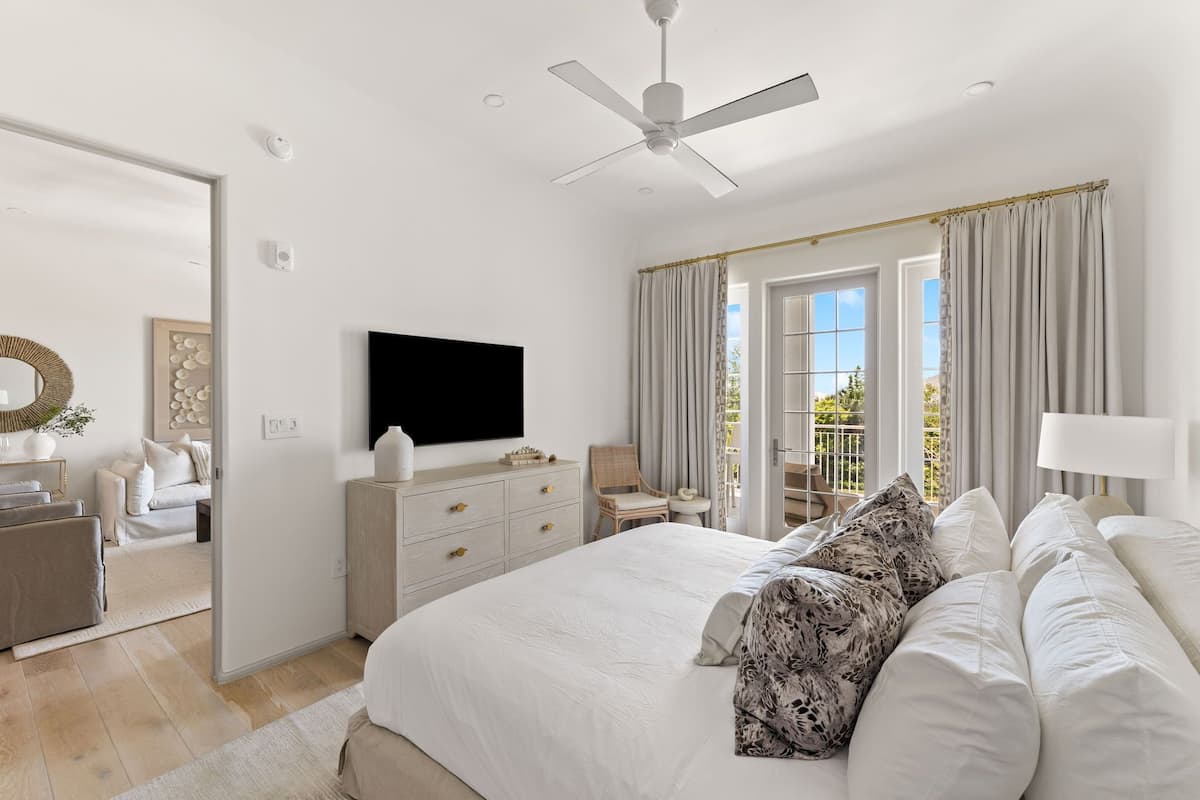 Un dormitorio con cama, televisor, ventilador de techo, cómoda y ventana con cortinas.
