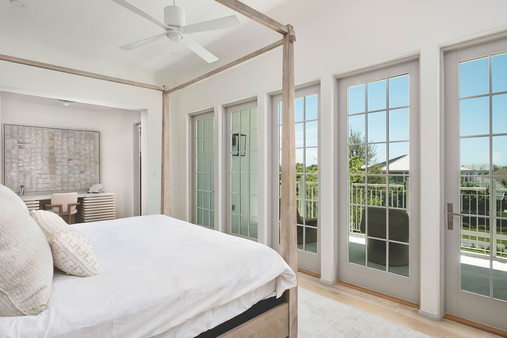Ein Schlafzimmer mit Himmelbett, Deckenventilator und großen Schiebetüren, die auf einen Balkon führen.