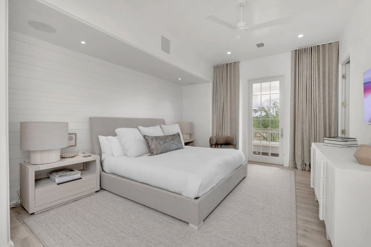 Un dormitorio moderno con una cama grande, mesitas de noche, un televisor y un balcón con cortinas.