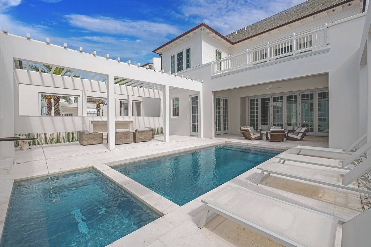 Un área de piscina moderna con dos piscinas, mobiliario exterior y un porche cubierto.