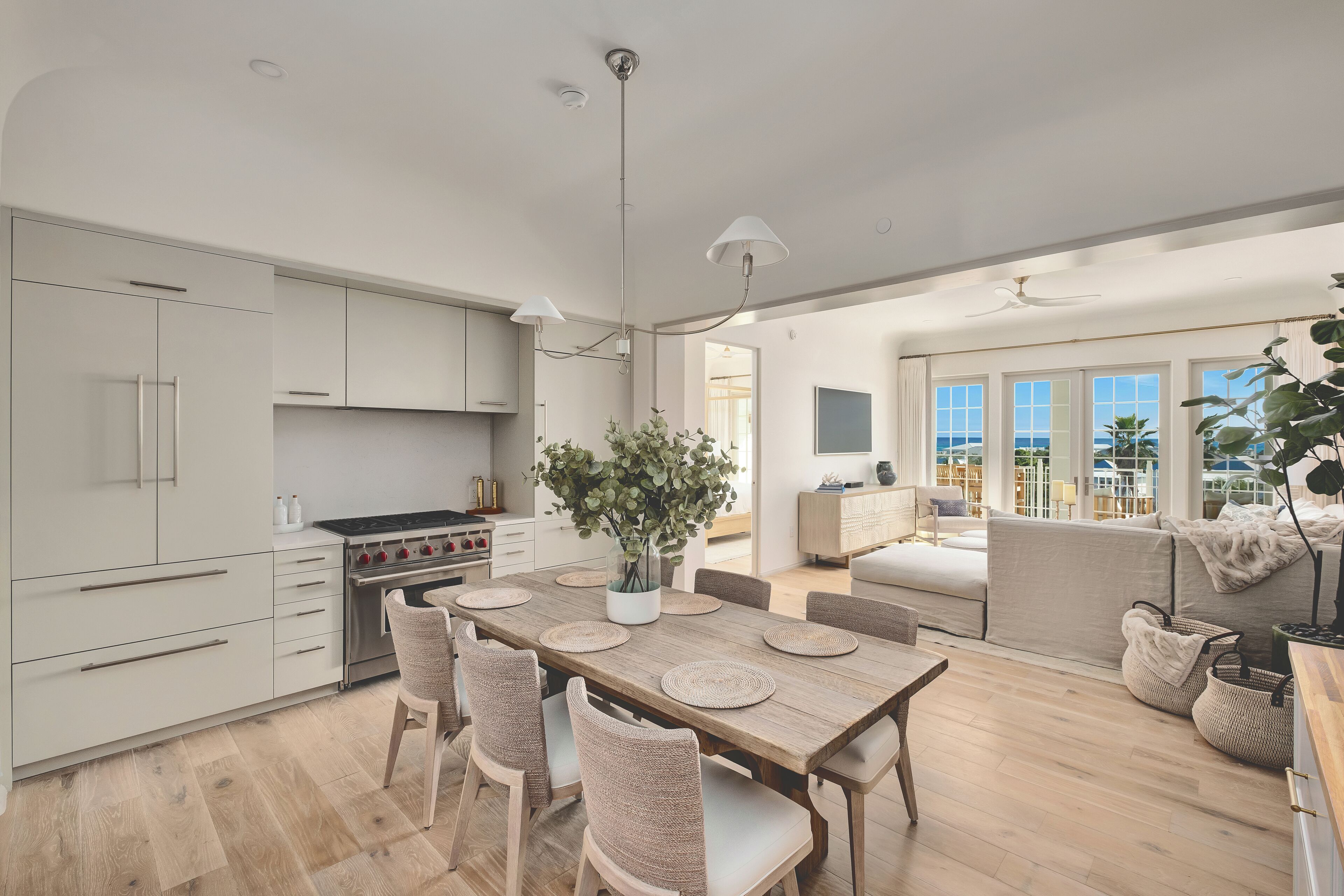 A modern kitchen with a dining area, large windows, and a view of the sea.