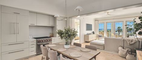 A modern kitchen with a dining area, large windows, and a view of the sea.