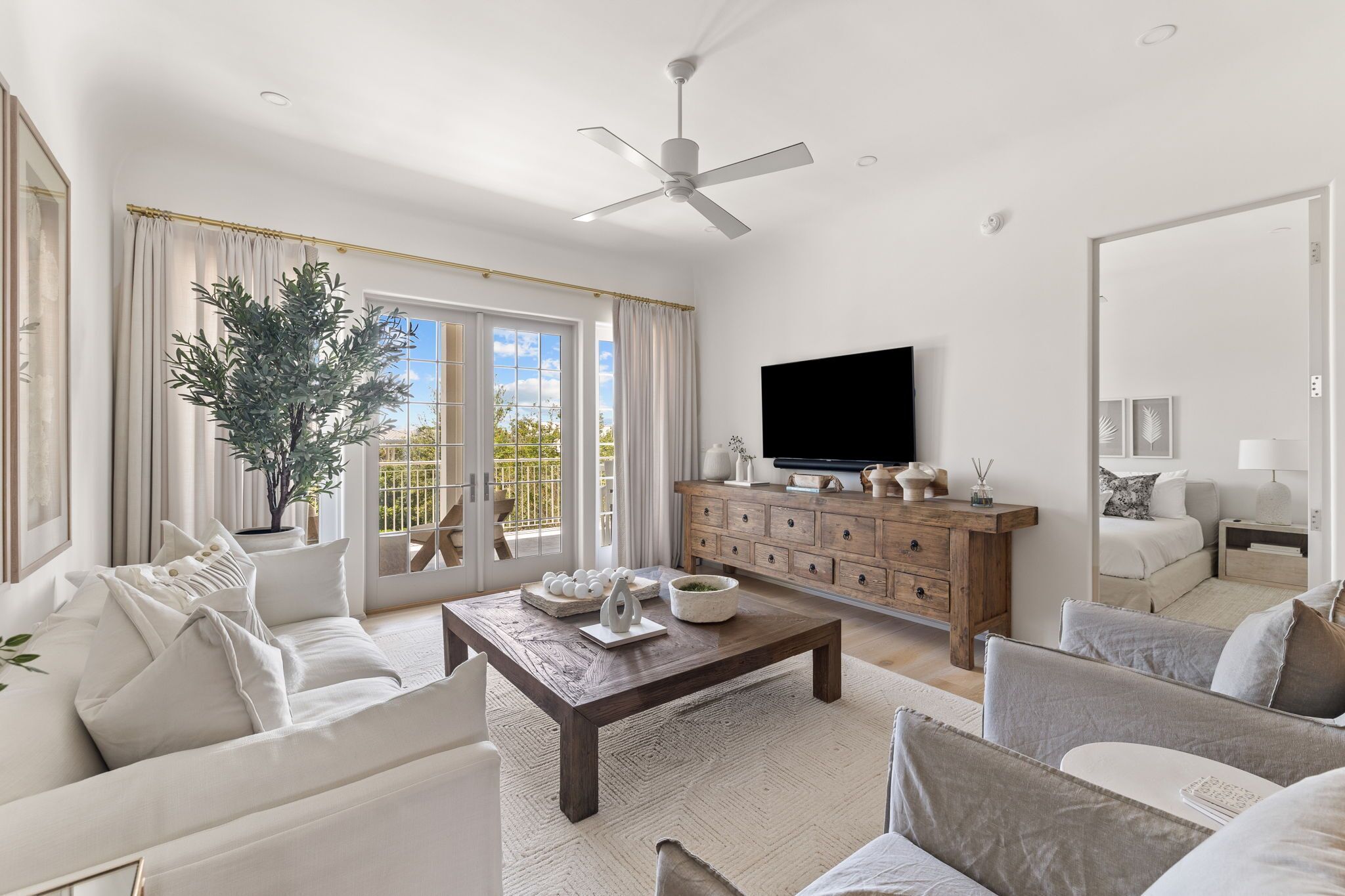 A spacious living room with a large window, a ceiling fan, a wooden coffee table, and a television.