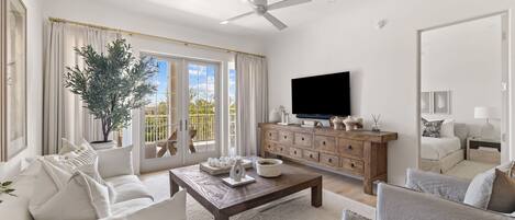 A spacious living room with a large window, a ceiling fan, a wooden coffee table, and a television.