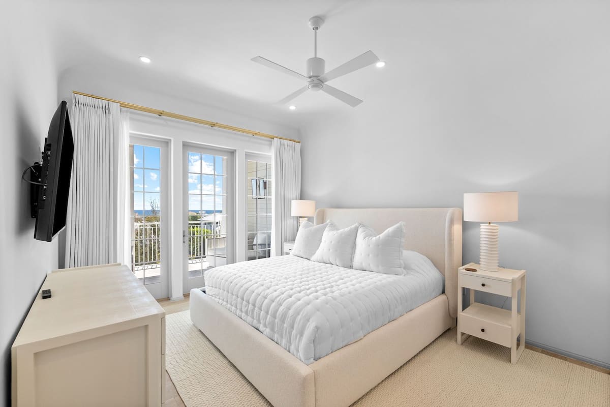 Un dormitorio con cama, mesitas de noche, ventilador de techo y vistas al exterior.