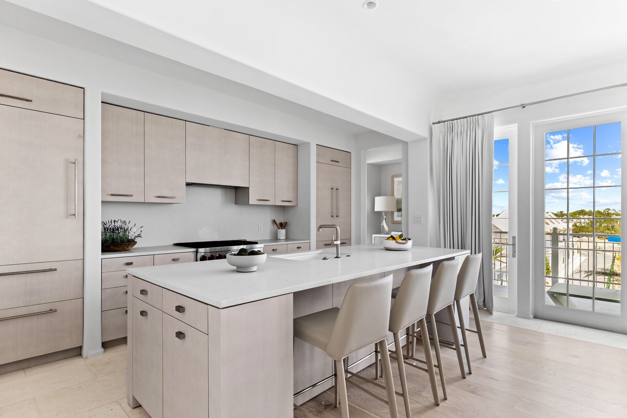 A modern kitchen with a central island, bar stools, and a large window with a view.