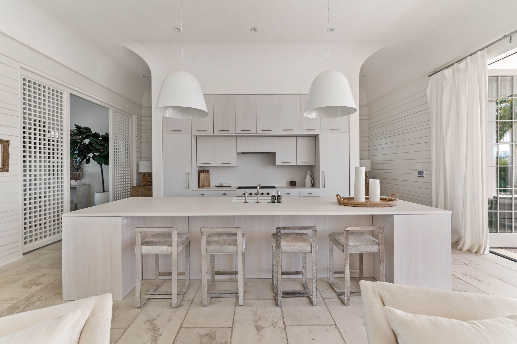 A modern kitchen with a central island, bar stools, pendant lighting, and a view of the outdoors.