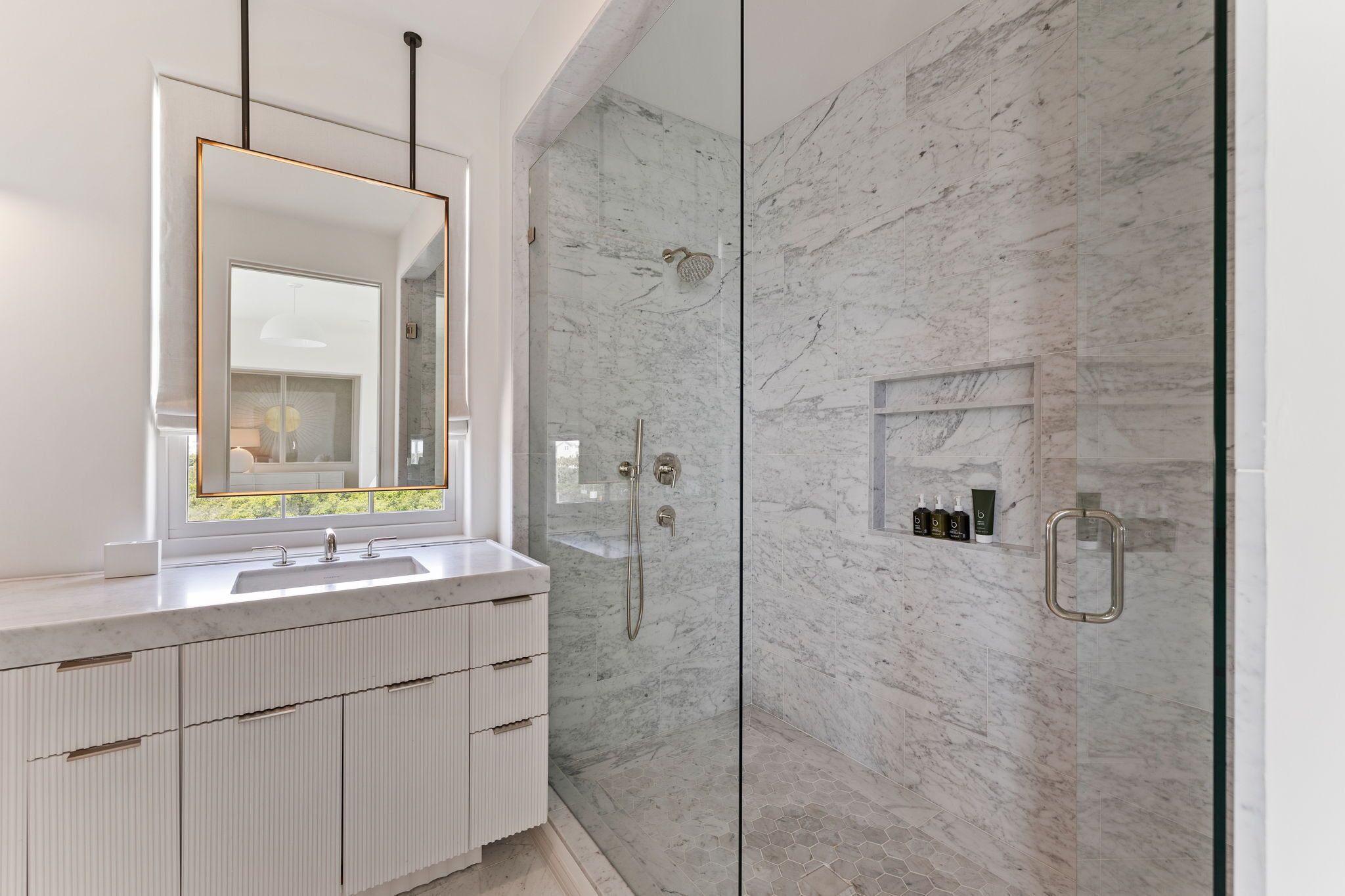 A modern bathroom with a large mirror, a shower with a glass door, and a marble wall.