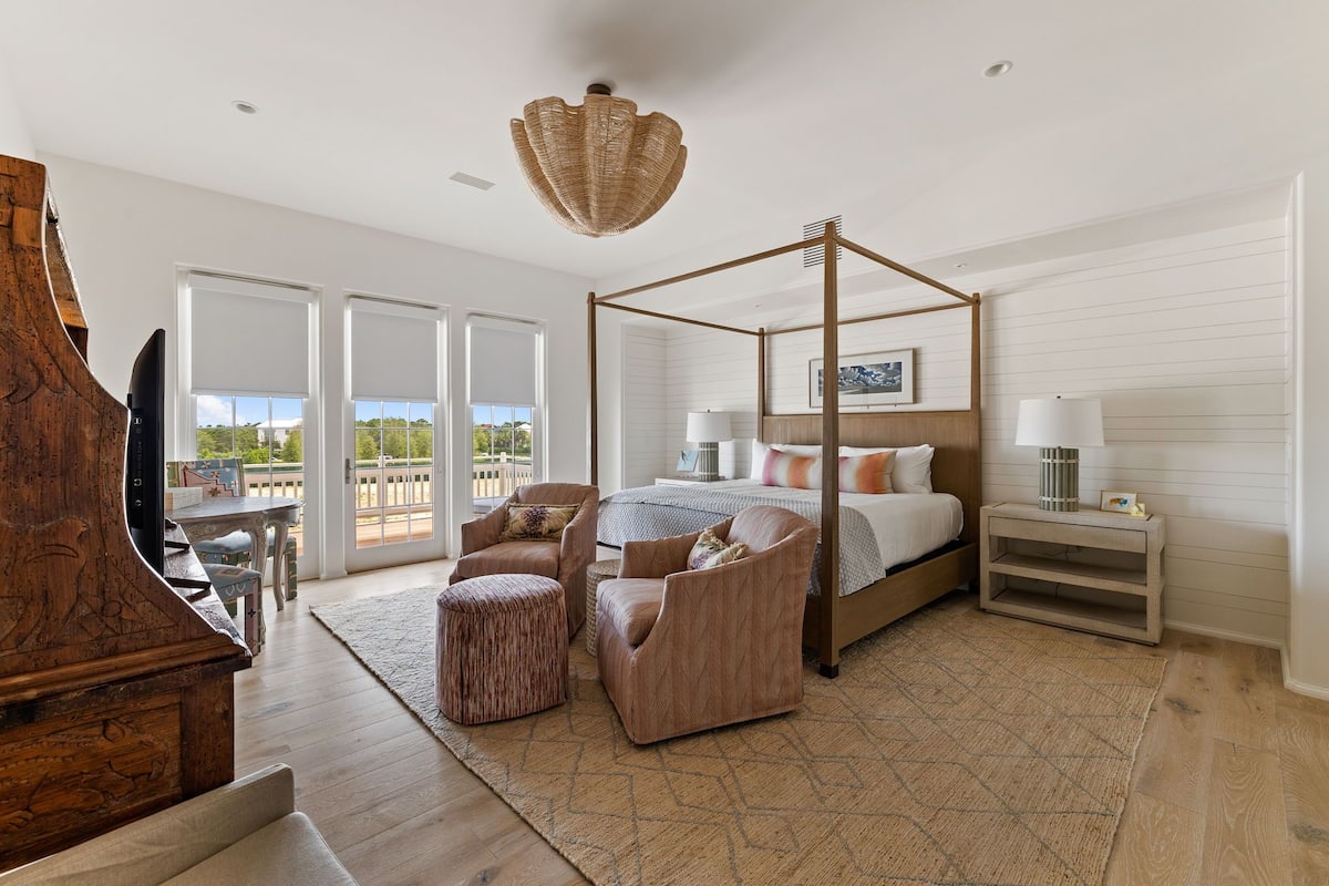 Un espacioso dormitorio con cama con dosel, un piano de madera y un amplio ventanal con vistas al exterior.