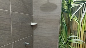 A bathroom with dark tiles, a shower head, a toilet, and a shower curtain with a leaf pattern. - La Perla del Caribe  (Riohacha)