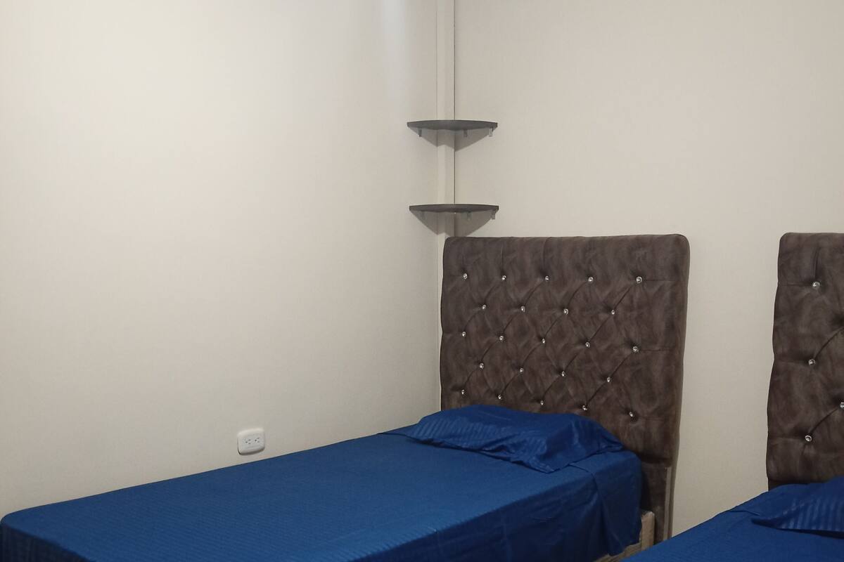 Une chambre avec deux lits simples, chacun doté d’une couvre-lit bleue et d’une tête de lit capitonnée.