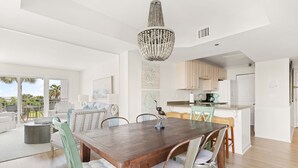 A spacious dining area with a wooden table and chairs, a chandelier, and a view of the outdoors. - Fall Special | Condo with pool, steps to the beach (St Simons Island)