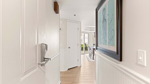 A hallway with white walls, a wooden floor, a door with a silver handle, and a framed artwork on the wall. - Fall Special | Condo with pool, steps to the beach (St Simons Island)