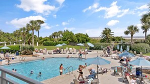 A pool area with lounge chairs and umbrellas, surrounded by palm trees and a clear sky. - Fall Special | Condo with pool, steps to the beach (St Simons Island)