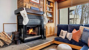 A cozy living room with a fireplace, wooden shelves, a blue sofa, and a view of the outside.