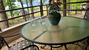A glass table with two wine glasses and a potted plant on a balcony with a view of trees and a building.