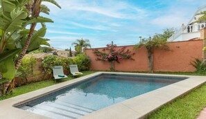 A rectangular swimming pool with a tiled edge, surrounded by a grassy area and a brick wall. There are two lounge chairs and a small table with a green cushion. - Traditional 4BR Spanish villa with a lot of character close to Puerto Banus. (Marbella)