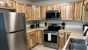 A modern kitchen with wooden cabinets, stainless steel appliances, and a tiled floor.