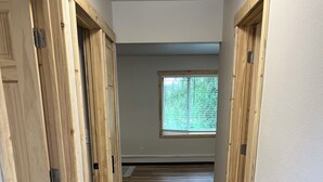 A hallway with wooden flooring and doors, leading to a room with a window.