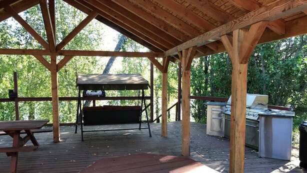 A covered outdoor area with a picnic table, a grill, and a barbecue station.