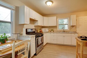 A kitchen with white cabinets, a stove, oven, microwave, and a window.