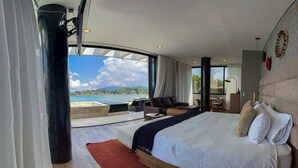A modern hotel room with a large bed, a seating area, and a view of the sea.