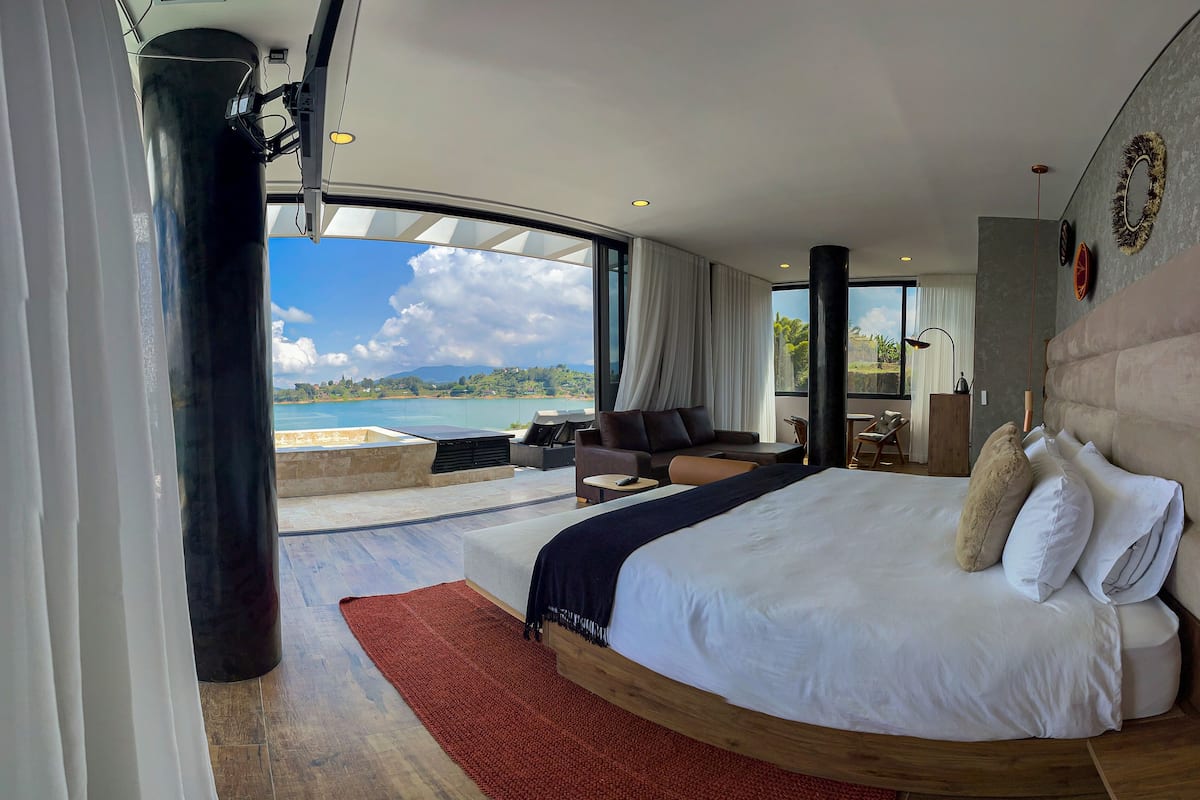 A modern hotel room with a large bed, a seating area, and a view of the sea.