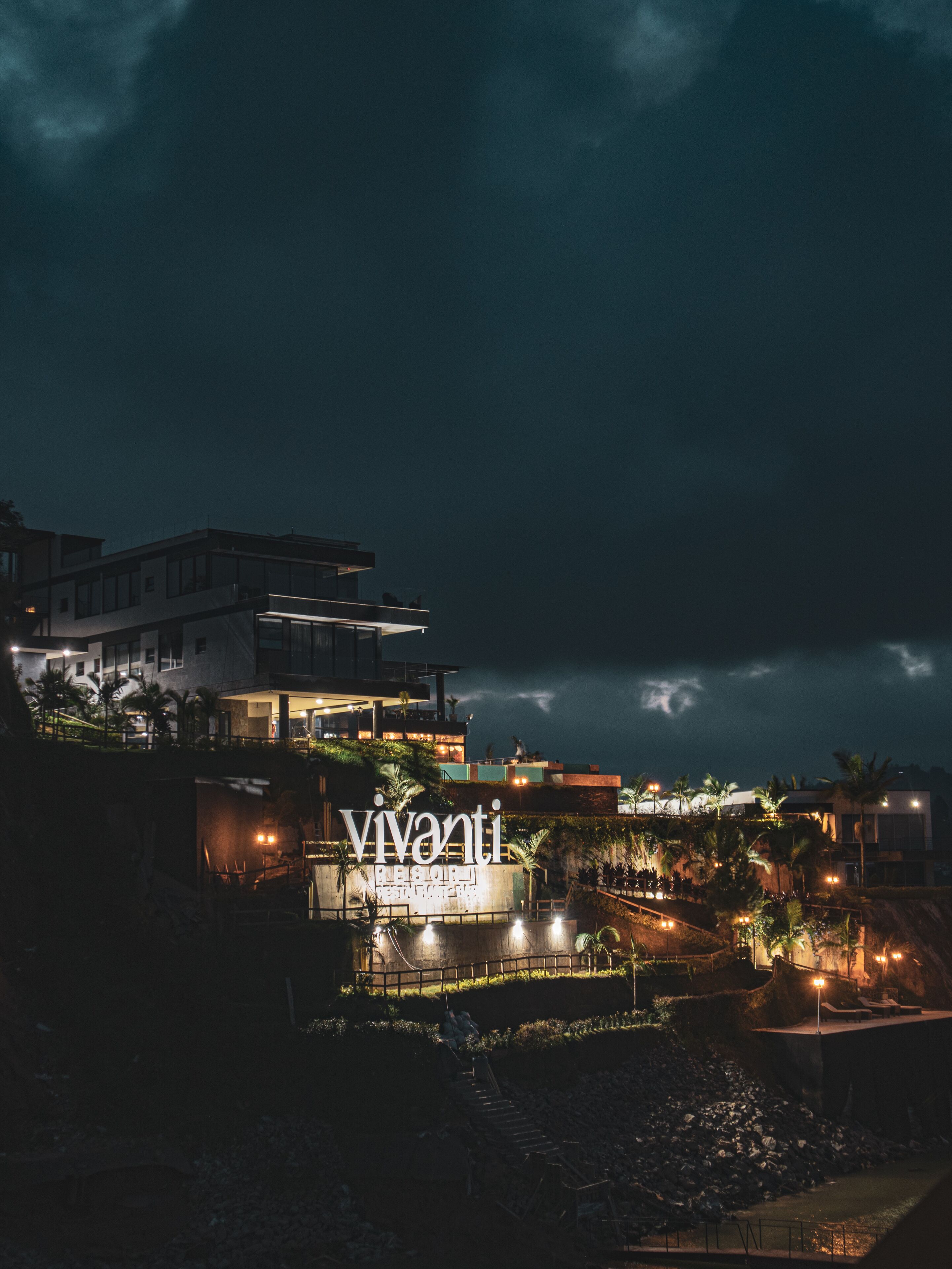 Un hotel moderno con un llamativo letrero iluminado, un jardín ajardinado y vistas del entorno.