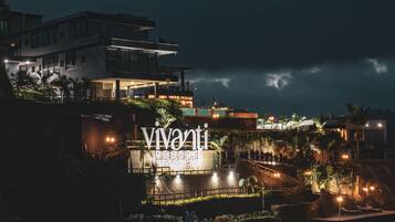 Un hotel moderno con un llamativo letrero iluminado, un jardín ajardinado y vistas del entorno.