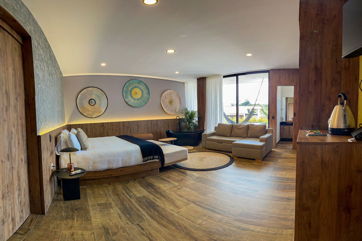 A modern hotel room with a large bed, a sofa, a coffee table, and a dining area.
