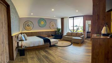 A modern hotel room with a large bed, a sofa, a coffee table, and a dining area.