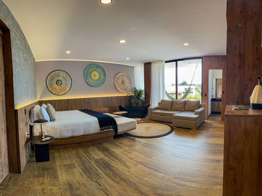 A modern hotel room with a large bed, a sofa, a coffee table, and a dining area.