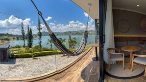 A hammock on a balcony overlooking a scenic landscape with trees and a body of water.