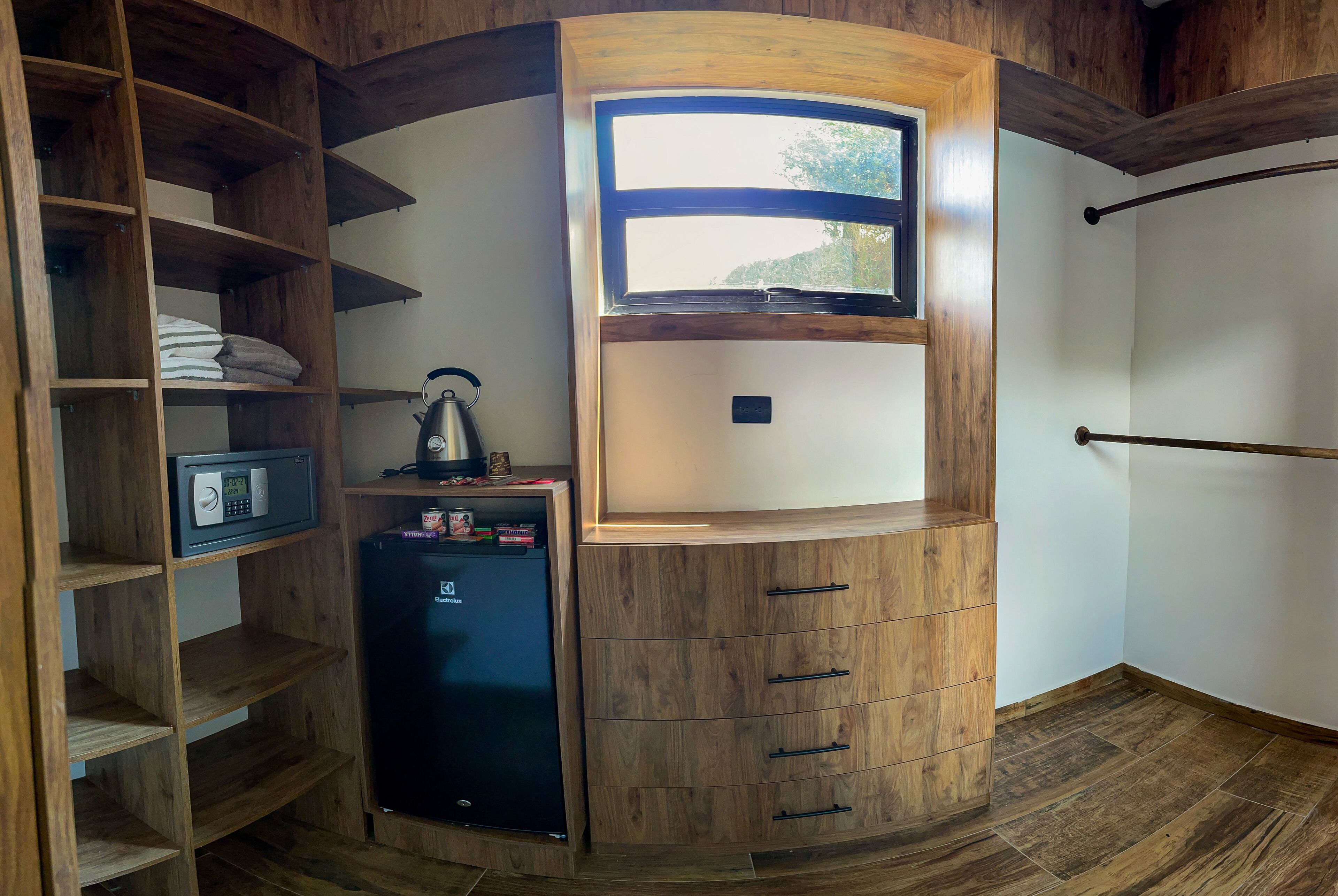 A compact room with a built-in wardrobe, a small refrigerator, and a window providing natural light.