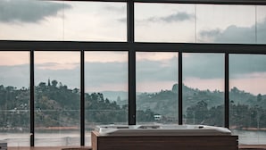 A bedroom with a large window overlooking a scenic landscape, a wooden bench, and a bathtub.