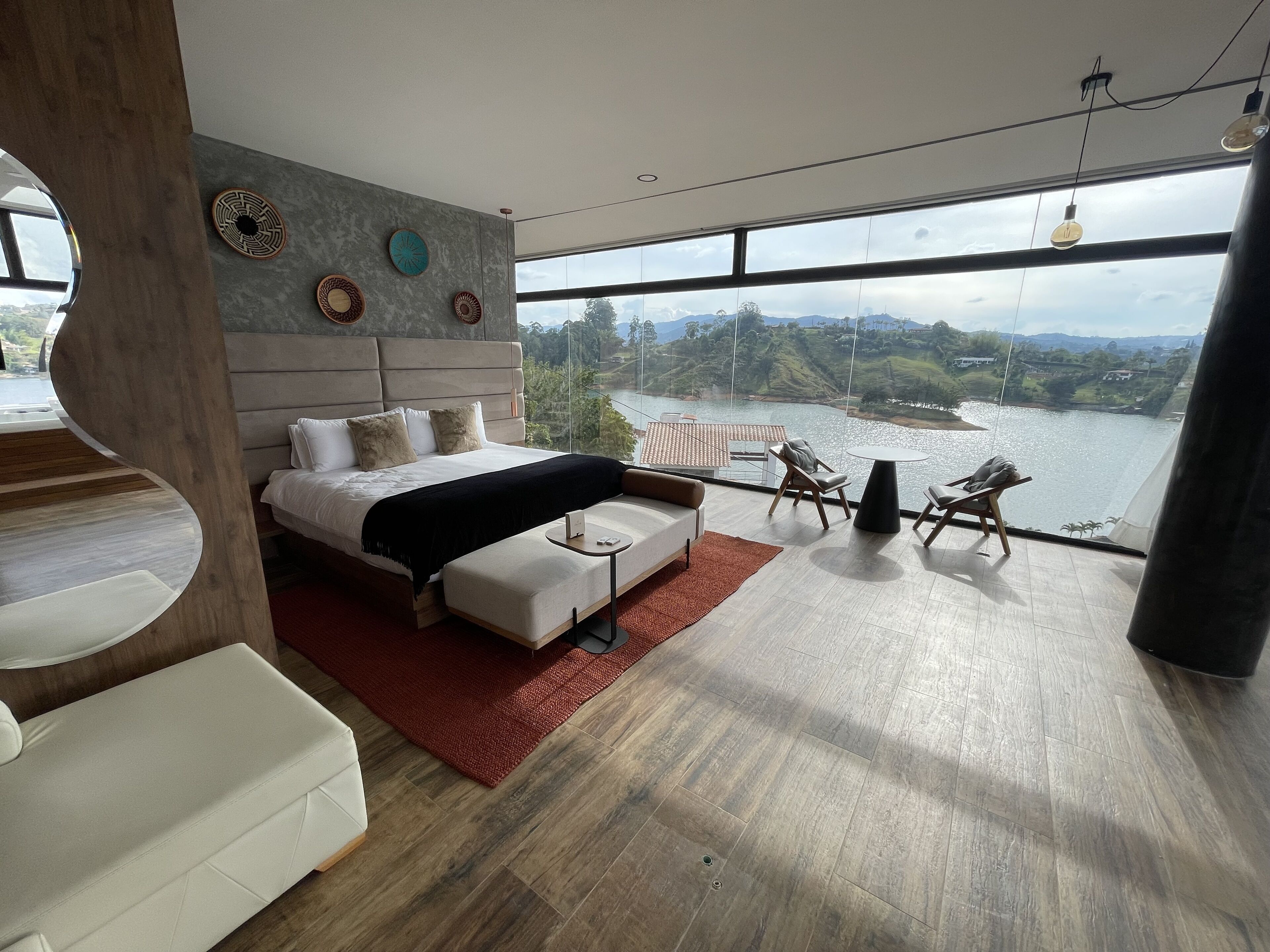 Un dormitorio moderno con una cama grande, vistas a un lago y un balcón con mobiliario.