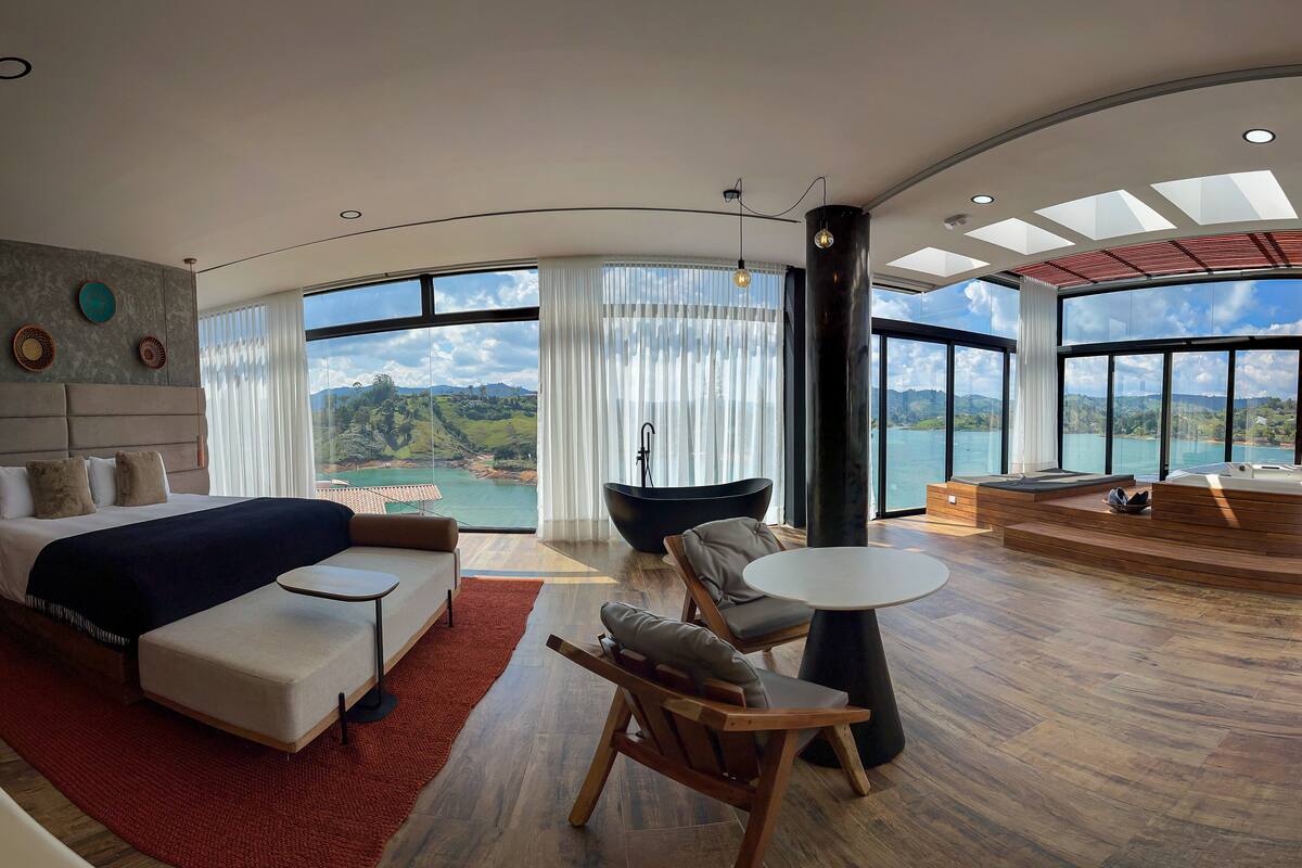 A modern hotel room with a large bed, seating area, and a view of the sea.