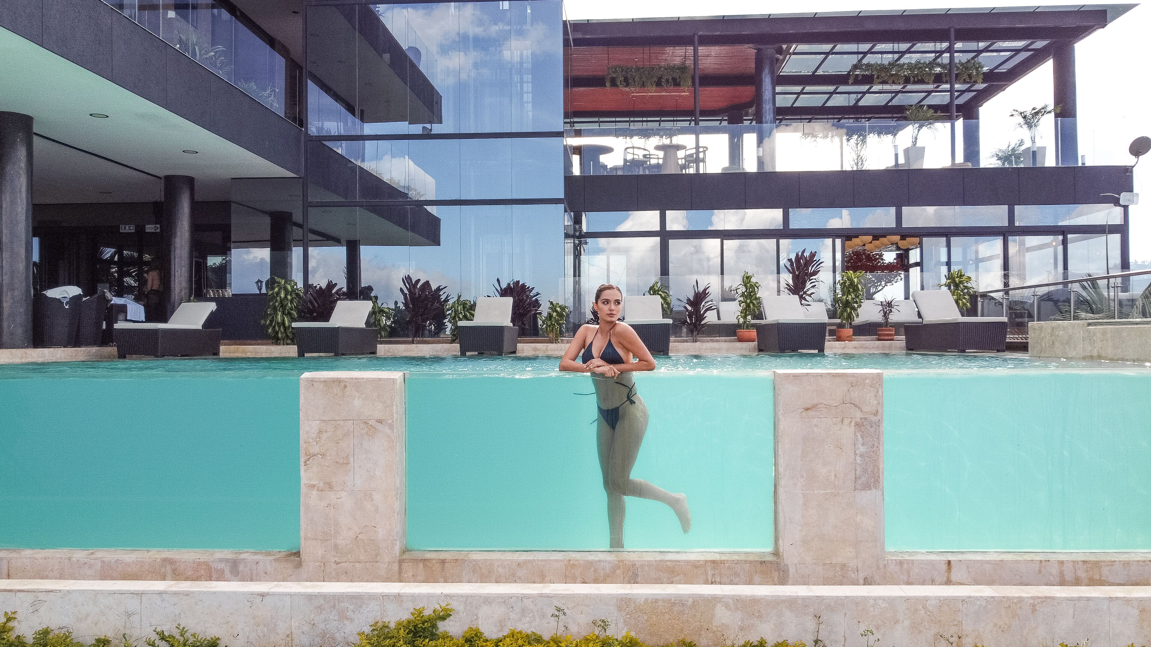 A pool area with lounge chairs and potted plants, surrounded by modern buildings with large windows.