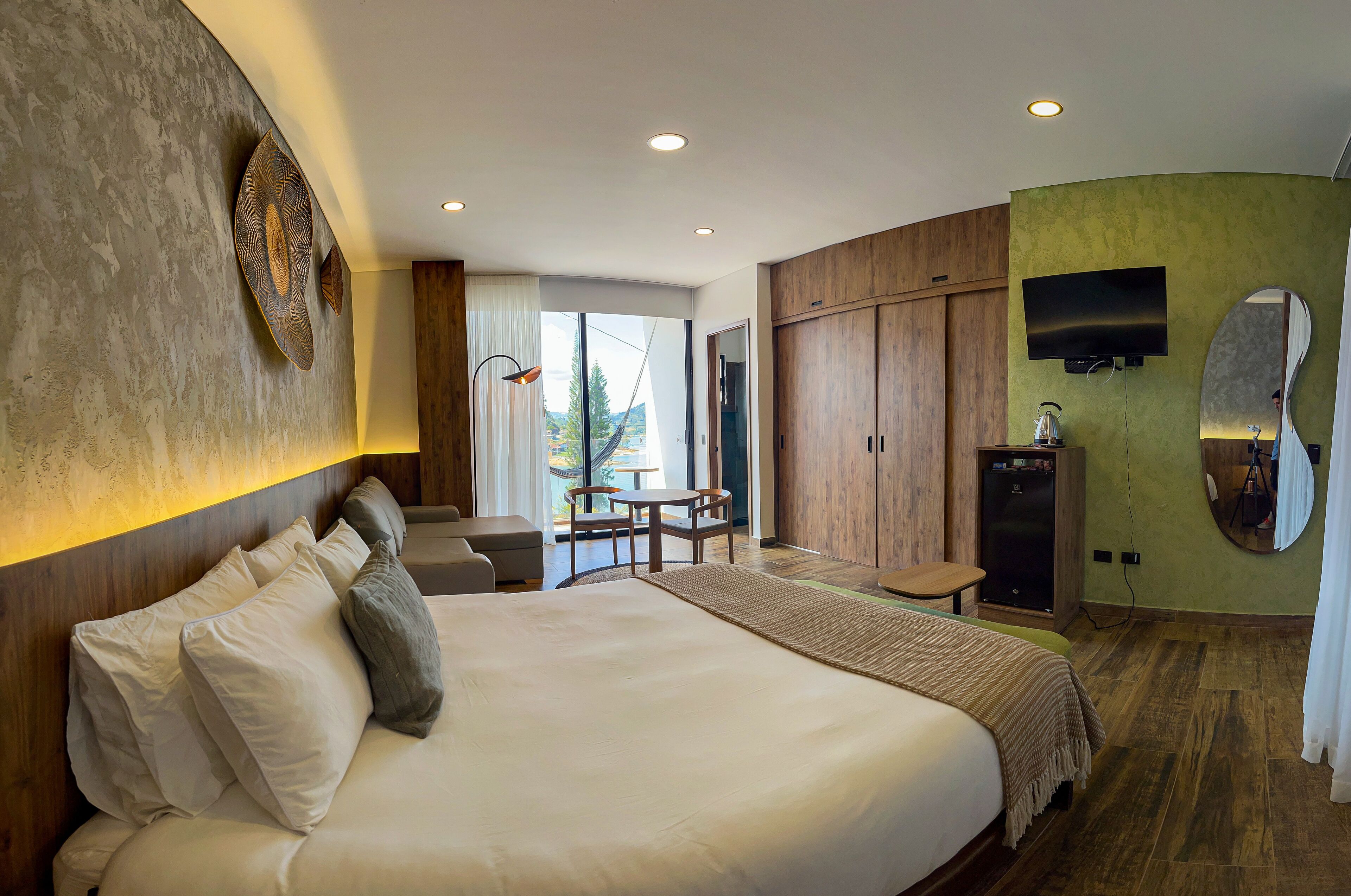 Una habitación de hotel moderna con una cama grande, un escritorio, un televisor y vistas al exterior.
