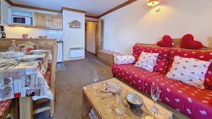 Ein gemütliches Wohnzimmer mit einem roten Sofa, einem Holztisch und einem Essbereich für vier Personen.