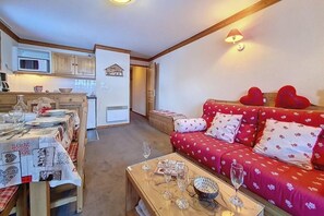 A cozy living room with a red sofa, a wooden coffee table, and a dining area with a table set for four. - 100m from shops, 1st floor, balcony, tv, ski locker, 44m², Les Menuires (Les Menuires)