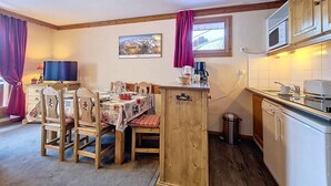 Eine gemütliche Küche mit Holzausstattung, einem Esstisch mit Stühlen, einer Mikrowelle und einem Fenster mit Vorhängen.