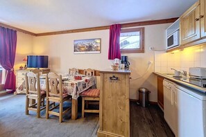 A cozy kitchen with wooden cabinets, a dining table with chairs, a microwave, and a window with curtains. - 100m from shops, 1st floor, balcony, tv, ski locker, 44m², Les Menuires (Les Menuires)