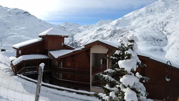 Eine Holzhütte mit Balkon, umgeben von schneebedeckten Bergen.