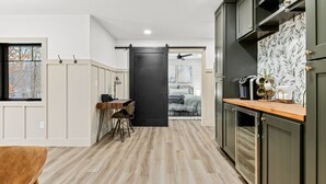 Une cuisine moderne avec un plancher en bois, un coin repas avec une table et des chaises, et une porte coulissante donnant sur une chambre.