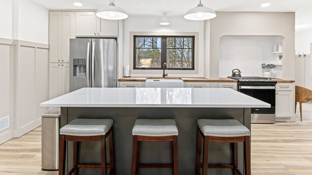 Une cuisine moderne dotée d’un grand îlot central, de tabourets de bar, d’appareils électroménagers en acier inoxydable et d’une fenêtre offrant une vue agréable.