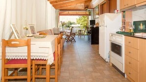A covered dining area with wooden tables and chairs, a kitchen with wooden cabinets, and a view of the outdoors.