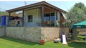 A stone house with a tiled roof, a glass door, and a small garden area with a slide and a green umbrella.