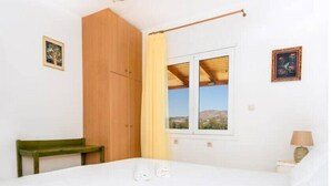 A bedroom with a bed, a wooden wardrobe, a bench, a window with a view, and a lamp.